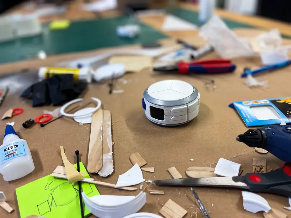 A white model of Senzu on a workbench among glue, pliers and offcuts